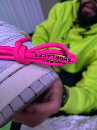 a man is holding up a pair of sneakers with a pink laces